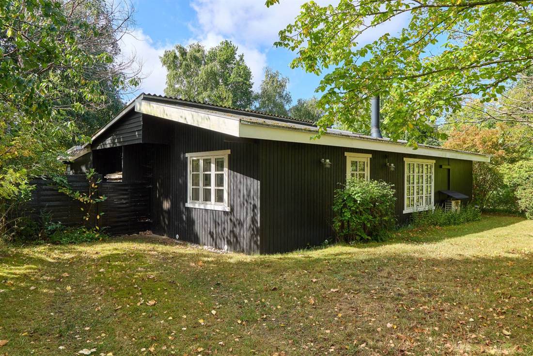 Ældre sommerhus med sort træbeklædning, hvide sprossede vinduer og bølgeplader på taget